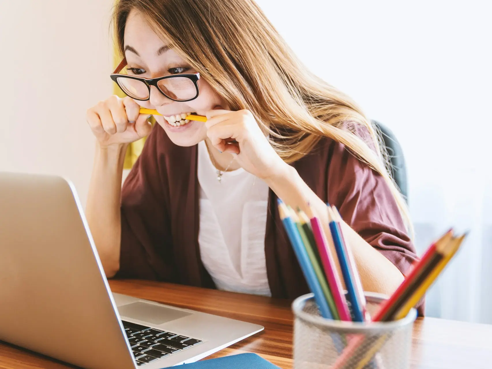 woman biting pencil while sitting on chair in front of computer during daytime